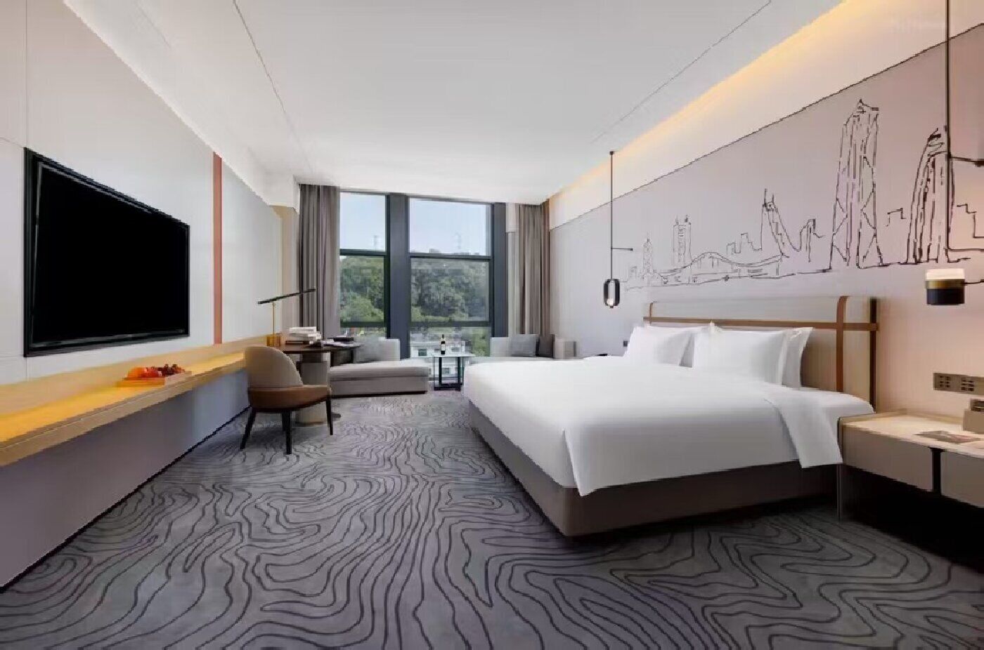A modern hotel room with a large bed, a desk, a chair, and a television.