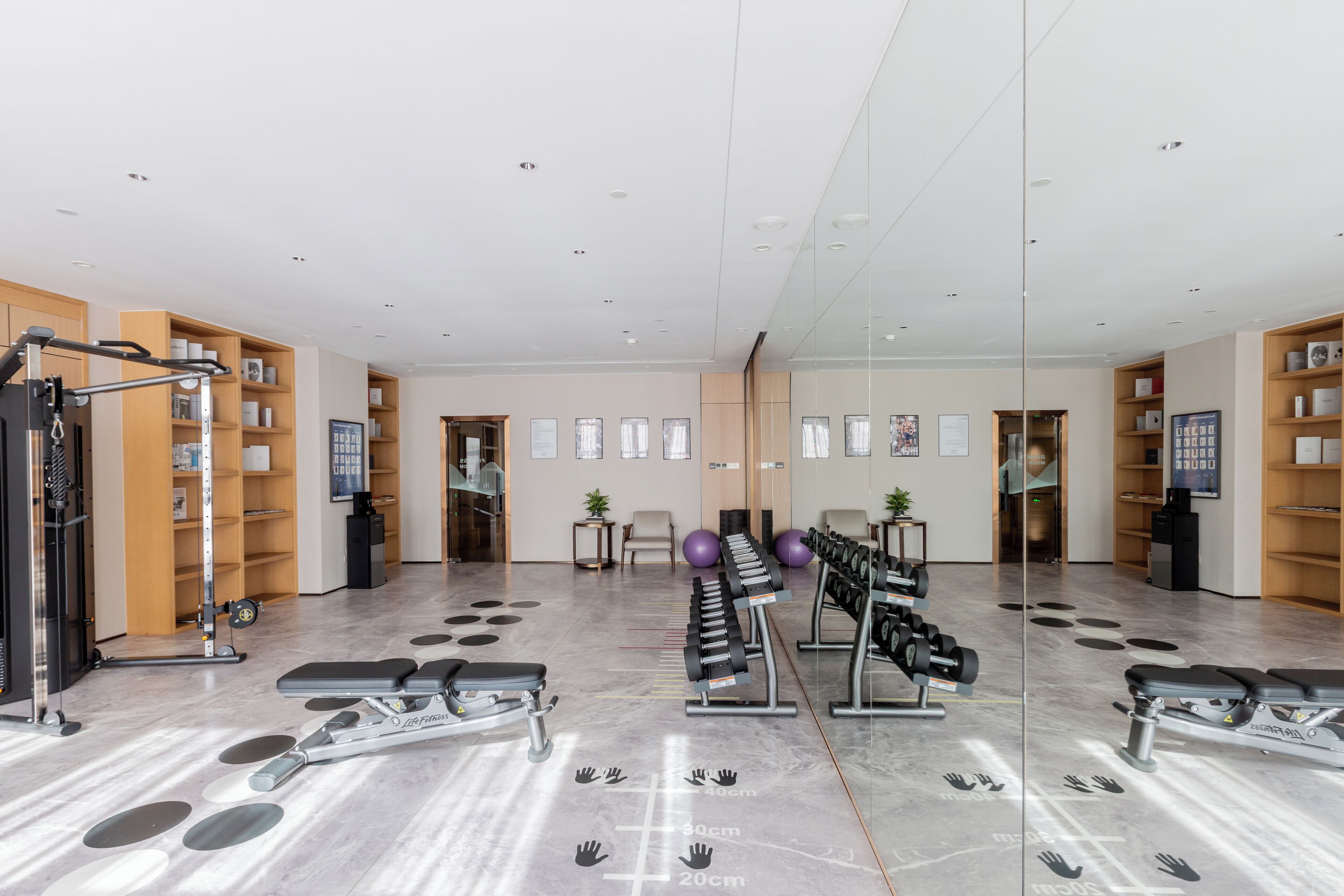 Une salle de sport équipée de matériel d’exercice, dotée de murs couverts de miroirs et de rayonnages en bois où sont disposés divers objets.