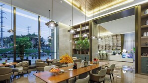 Un'area pranzo moderna con un lungo tavolo in legno, sedute confortevoli, illuminazione a sospensione e vista sulla strada.