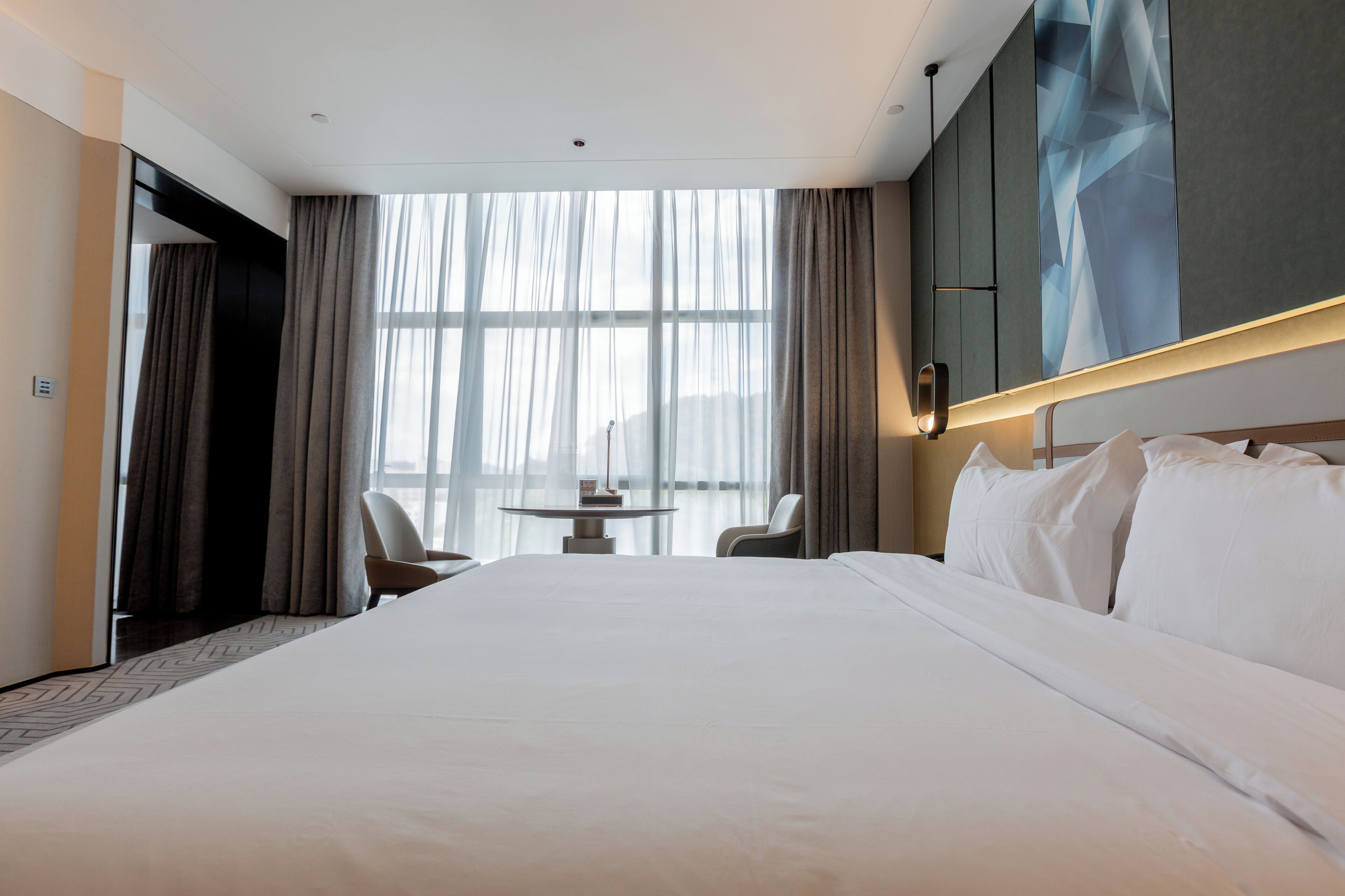 A modern hotel room with a large bed, a small round table, and two chairs.