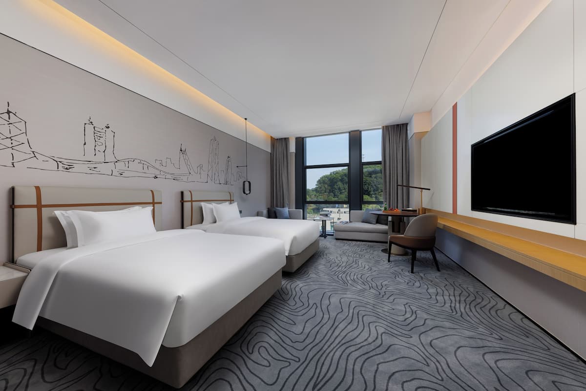 A hotel room with two beds, a sofa, a TV, and a large window with a view.