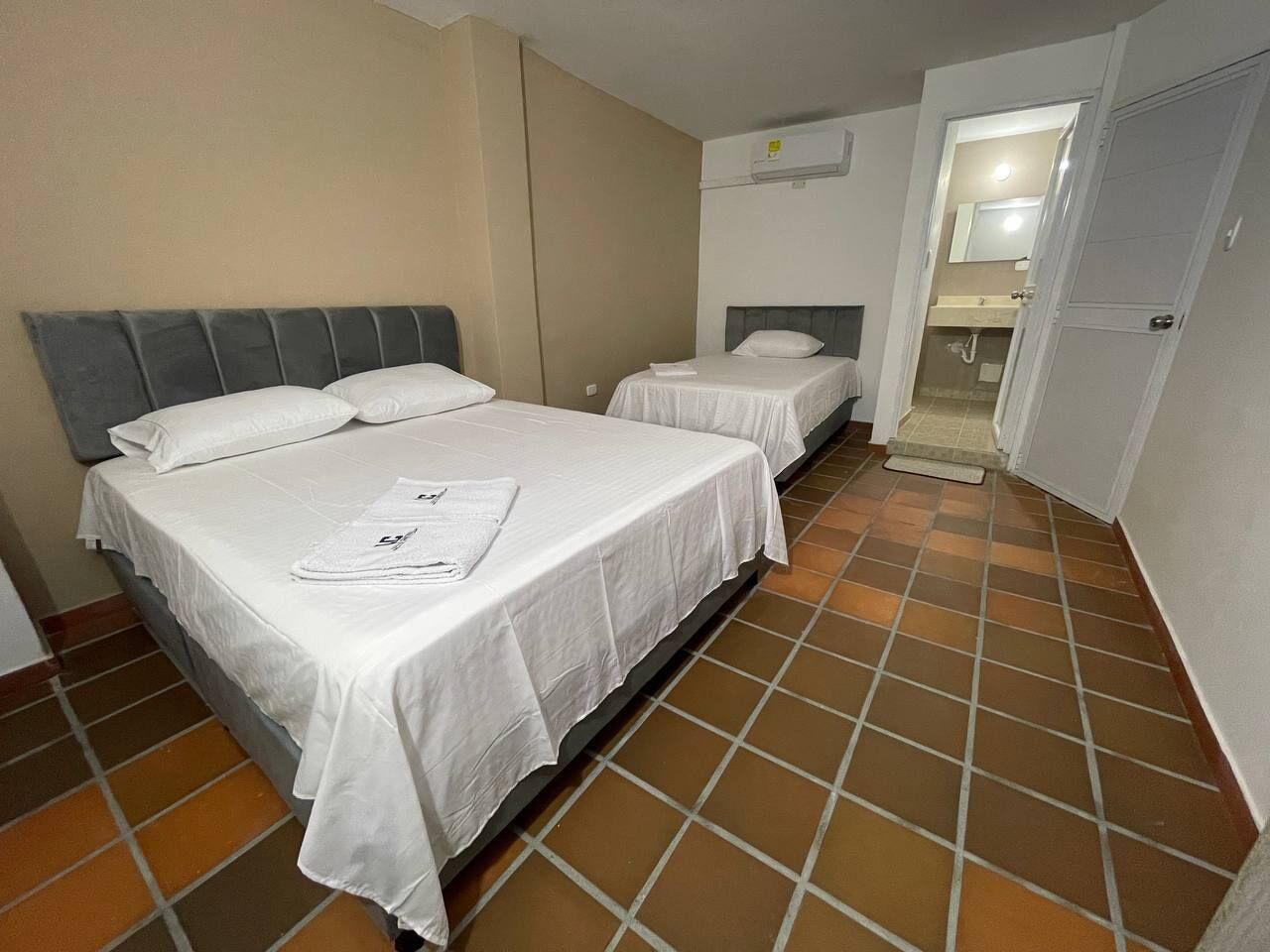 Een hotelkamer met twee bedden, een badkamer met douche en een betegelde vloer.