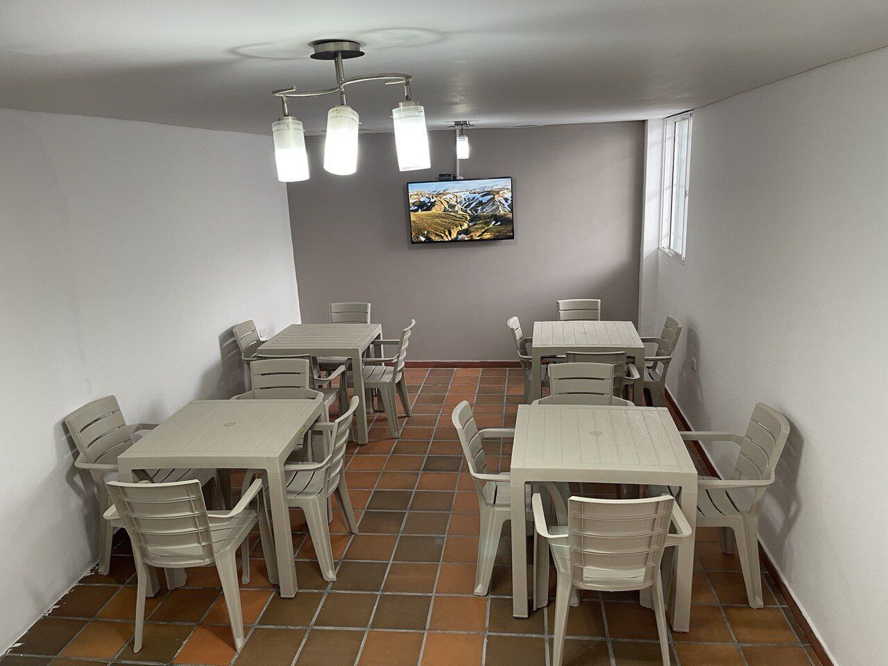 A dining area with multiple tables and chairs, a television mounted on the wall, and a ceiling light fixture.