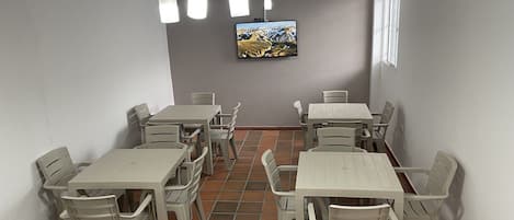 Un comedor con varias mesas y sillas, un televisor montado en la pared y una lámpara de techo.