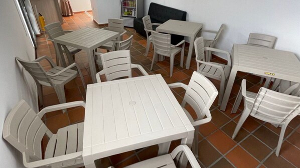A dining area with multiple white plastic tables and chairs, a refrigerator, and a black couch. - Hotel Valle Central (Valledupar)