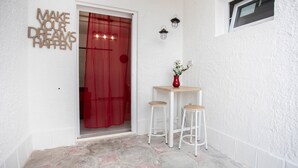 A small, clean entrance with a red door, a wall-mounted sign saying "MAKE YOUR DREAMS HAPPEN", and a small table with stools. - Piccola Stella | studio apartment in Torre Lapillo (Porto Cesareo)