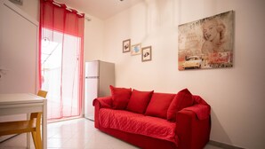 A compact living space with a red sofa, a white table, and a refrigerator. - Piccola Stella | studio apartment in Torre Lapillo (Porto Cesareo)