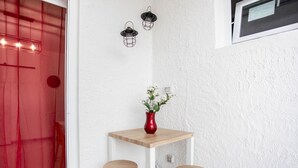 A small, white-walled room with a wooden table and two stools, a red vase with flowers, and three wall-mounted lanterns. - Piccola Stella | studio apartment in Torre Lapillo (Porto Cesareo)