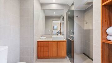 A modern bathroom with a wooden vanity, a white toilet, and a glass shower enclosure.