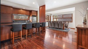 Een moderne keuken met houten kastjes, een bar met krukken, en een eethoek met tafel en stoelen.