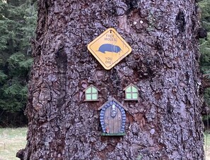 Un árbol con un letrero amarillo que dice “MOLES GRATIS, TÚ ESCAVA” y dos pequeñas casas adosadas al árbol.