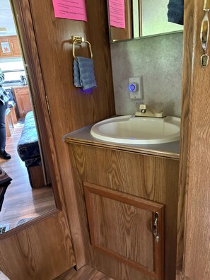 Un mueble de baño de madera con lavabo, una toalla colgada en un perchero y un espejo sobre el lavabo.