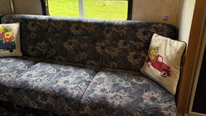 A sofa with floral upholstery and two decorative pillows, one with a floral design and the other with a vintage car and text. - 1-bedroom camper trailer minutes from Olympic Peninsula (Forks)