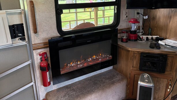A cozy RV interior with a fireplace, a television mounted on the wall, and a window overlooking a green landscape. - 1-bedroom camper trailer minutes from Olympic Peninsula (Forks)