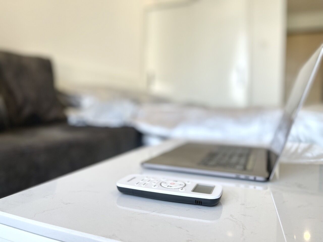 A laptop and a portable device on a white table in a hotel room.