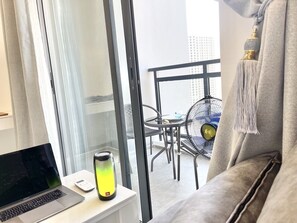 A modern room with a laptop on a desk, a standing heater, and a view of an outdoor balcony with chairs and a fan.