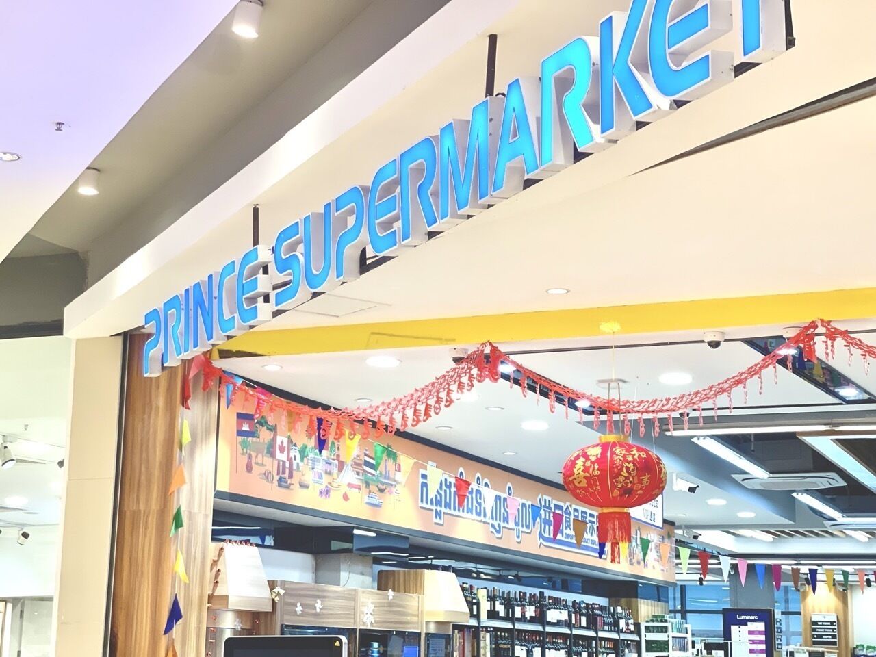 A supermarket entrance with a sign reading "PRINCES SUPERMARKET" and festive decorations.