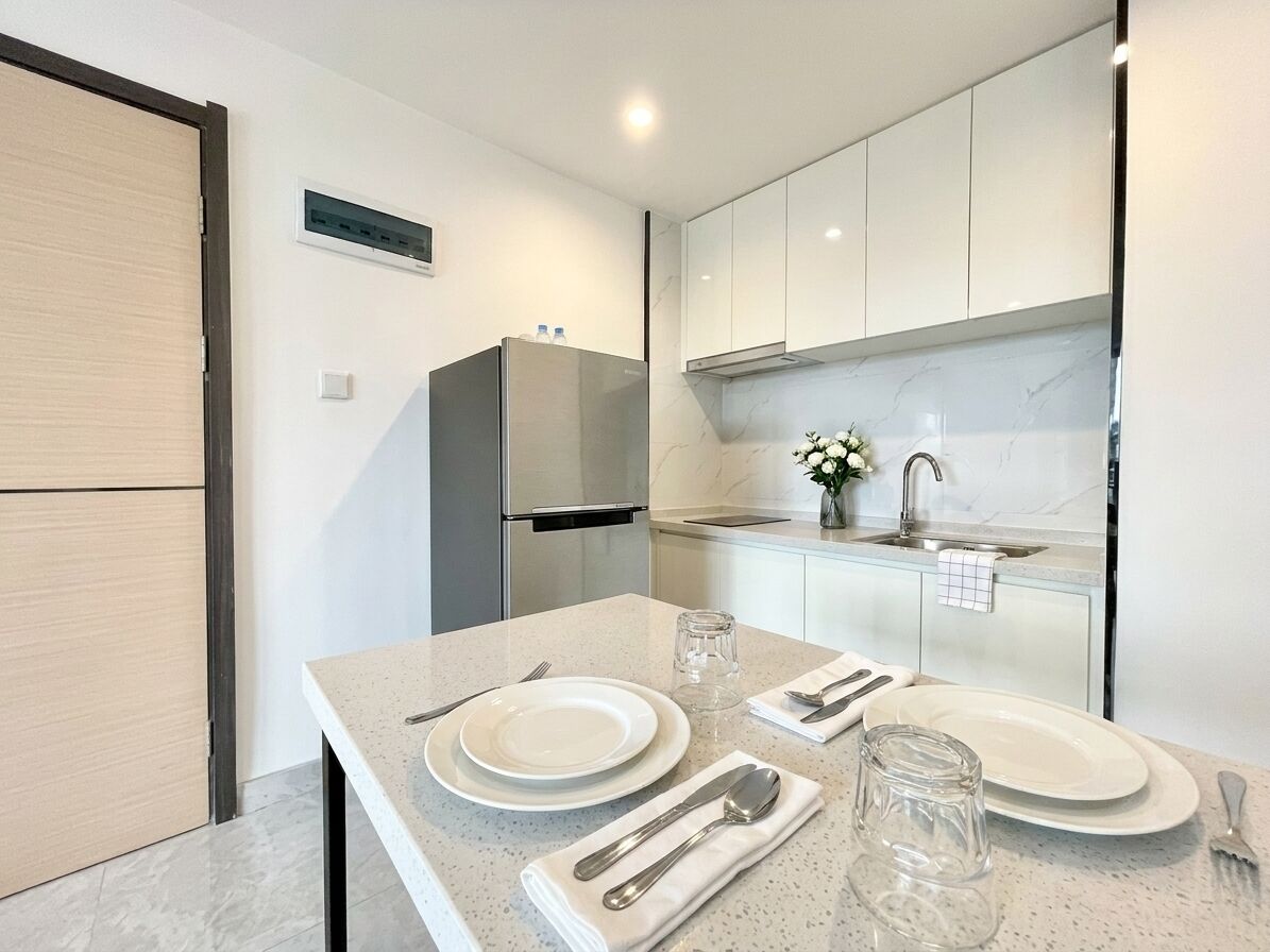A modern kitchen with white cabinets, a stainless steel refrigerator, and a marble countertop.