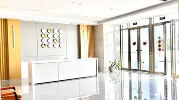 Una moderna zona de recepción con un mostrador blanco, un reloj montado en la pared y una entrada con puerta de cristal.