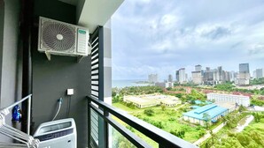 Varanda com unidade de ar condicionado e micro-ondas, com vista para um horizonte urbano repleto de edifícios e áreas verdes.