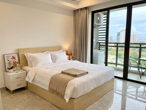 Una habitación de hotel moderna con una cama grande, una mesita de noche, una lámpara y vistas de la ciudad a través de amplios ventanales.