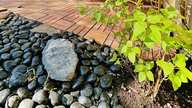 Una terraza de madera con una hamaca, una silla de madera y una planta en maceta.