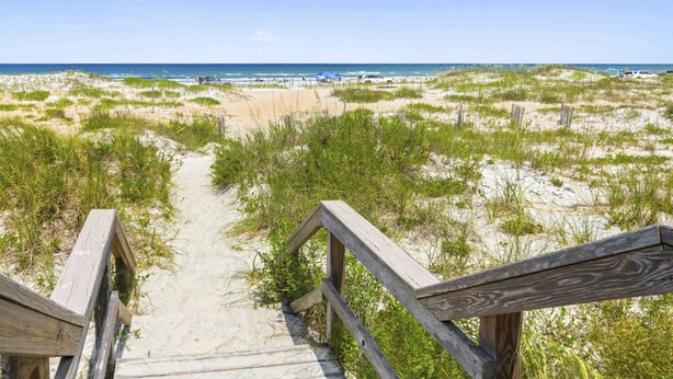 Een houten looppad dat naar een strand leidt, met duinen en schaarse begroeiing.