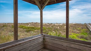 Een houten constructie met een bank, met uitzicht op een strand met duinen en schaarse begroeiing.