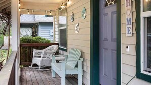 A porch with two rocking chairs, a string of lights, and a 'HOME' sign on the door. - Single Level Coastal Bungalow, Hot Tub, Pet Friendly, Fire Pit, Moments to Beach and Rockaway (Rockaway Beach)
