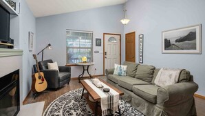 A living room with a sofa, a coffee table, a guitar, a fireplace, and a window with blinds. - Single Level Coastal Bungalow, Hot Tub, Pet Friendly, Fire Pit, Moments to Beach and Rockaway (Rockaway Beach)