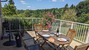 Un patio con una mesa lista para comer, rodeado de sillas y una parrilla.