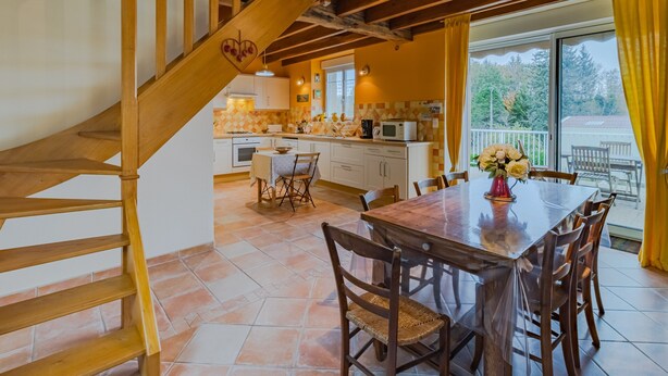 Una cocina con escalera de madera, un comedor con mesa y sillas, y vistas a través de un ventanal.