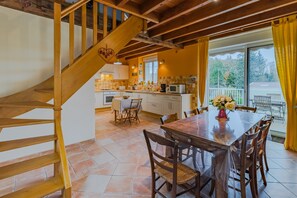 Une cuisine avec un escalier en bois, un coin repas avec une table et des chaises, et une vue à travers une porte vitrée.