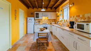 Una cocina con armarios blancos, salpicadero de azulejos, una mesa de comedor con sillas y un microondas.