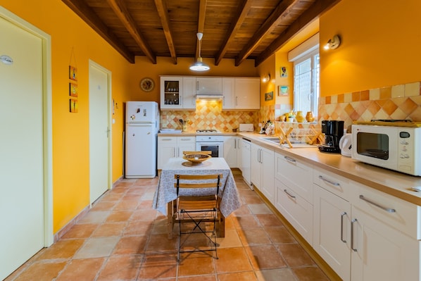 Une cuisine avec des meubles blancs, un plan de travail recouvert de carreaux, une table à manger avec des chaises et un four à micro-ondes.