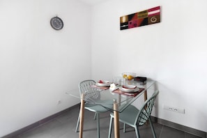 Un coin repas comprenant une table en verre, deux chaises, une horloge murale et une œuvre d’art encadrée.