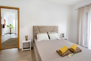 Une chambre d’hôtel avec un lit, deux tables de chevet, un miroir, une plante en pot et une vue sur le couloir.