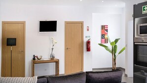 En moderne stue med sofa, fjernsyn, en trædør, et lille bord med en vase og en plante.