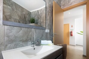Une salle de bain moderne avec un mur en marbre, un lavabo blanc et une porte en bois.