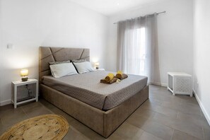 Une chambre à coucher avec un lit, des tables de chevet, une commode, une petite table d’appoint blanche et un tapis tissé.