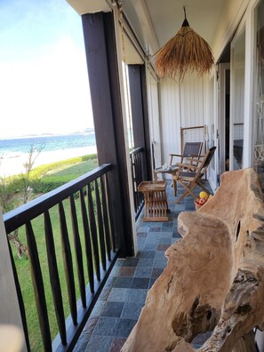 A balcony with a view of the ocean, a wooden chair, a small table, and a large tree stump.