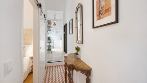 Un corridoio con pavimento in legno, un tavolo consolle con una pianta in vaso e opere d'arte appese al muro.