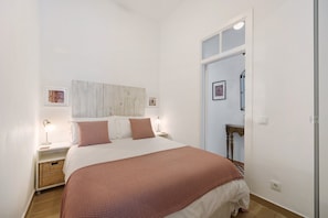 Een slaapkamer met een bed, nachtkastjes, een wandlamp, een houten hoofdbord en een deur naar een andere kamer.