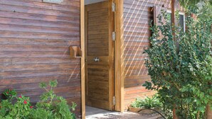 Una puerta de madera con un cartel arriba, un pequeño jardín con plantas y una valla de madera.