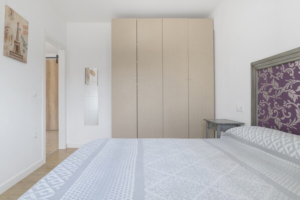 Un dormitorio con cama, armario, una mesita y un panel decorativo en la pared.
