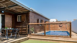 A wooden house with a fenced pool area, a table with chairs, and a small garden.