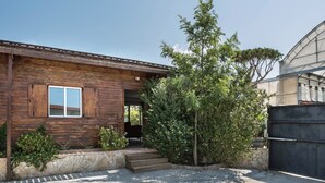 A wooden house with a porch, steps leading to the entrance, and a garden area with various plants.