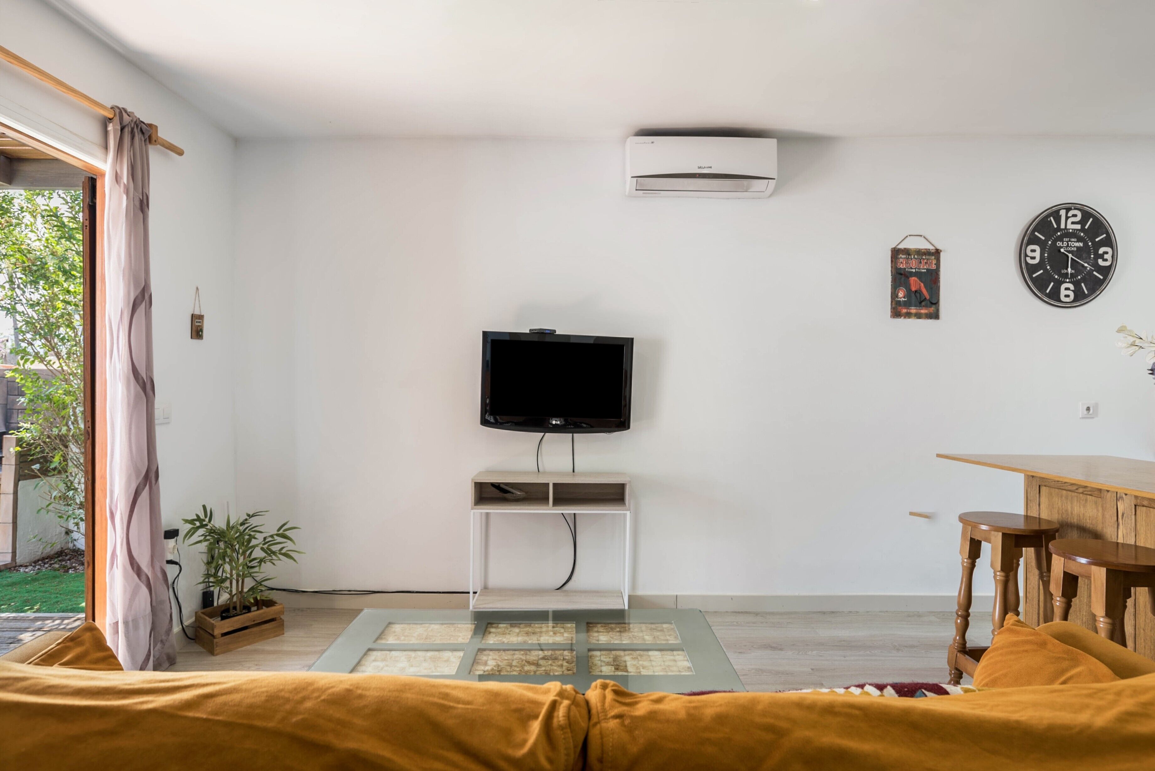 A living room with a television on a white stand, a clock, and a small table.