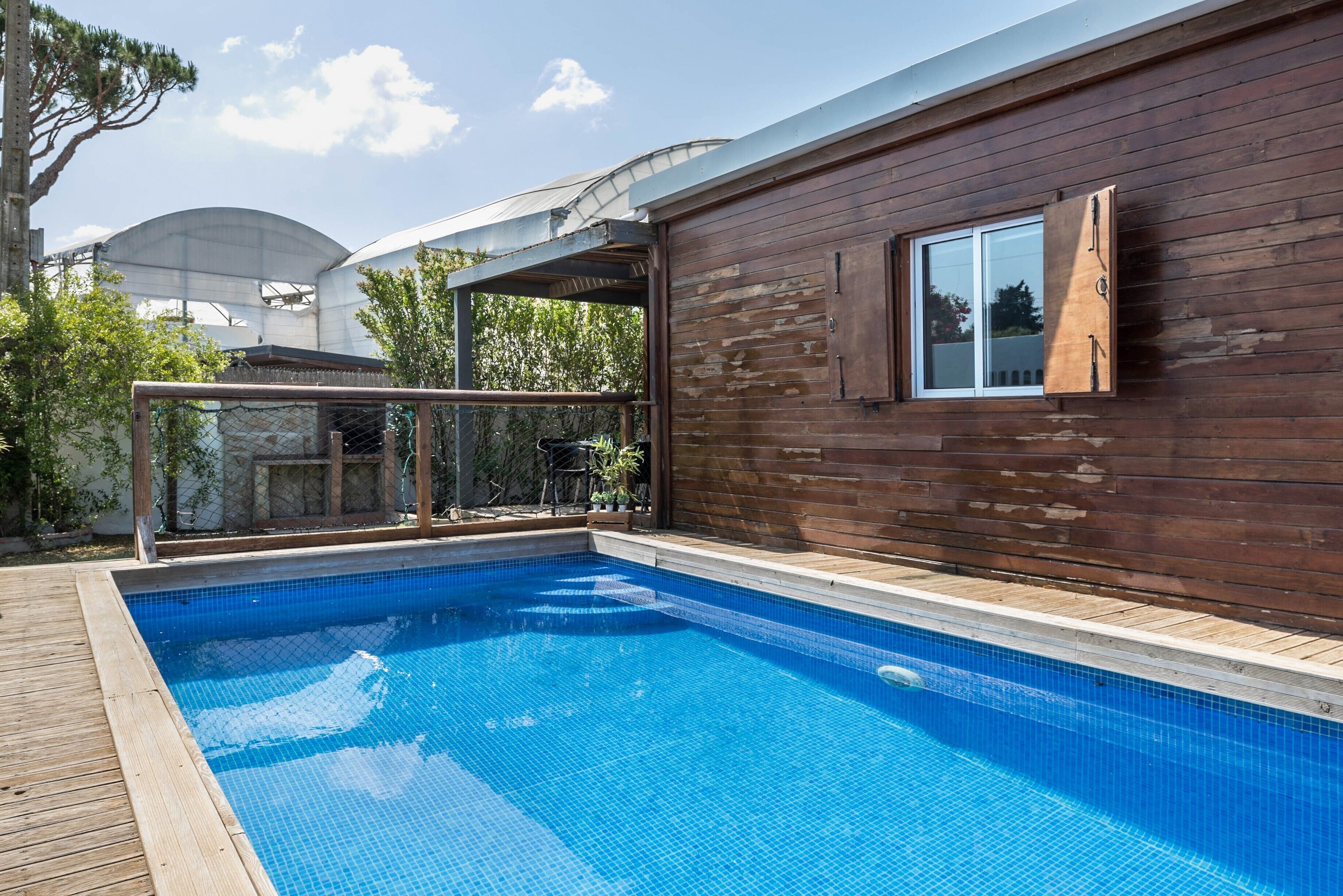 A swimming pool with a wooden deck, a glass balustrade, and a wooden exterior wall.