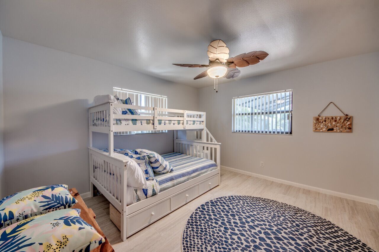 A child's bedroom with bunk beds, a ceiling fan, a window with blinds, and a patterned rug.
